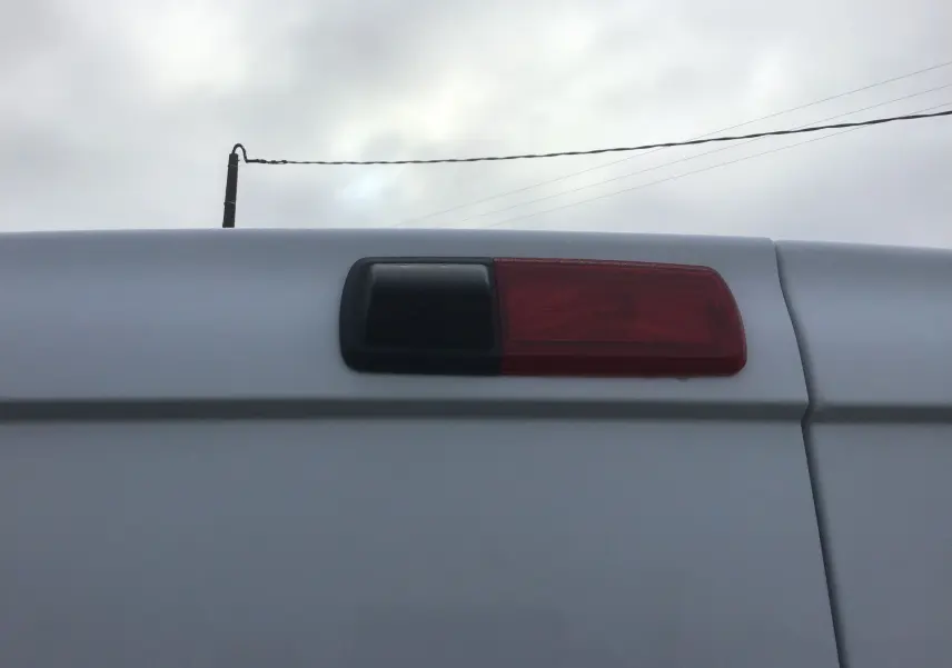 Gros plan sur la caméra de recul et feu stop arrière du Renault Trafic Fourgon blanc, partie haute de la porte arrière.