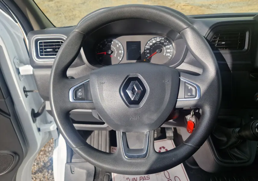 Vue intérieure centrée sur le volant noir Renault d’un Master Châssis Cabine blanc avec tableau de bord et clé insérée.