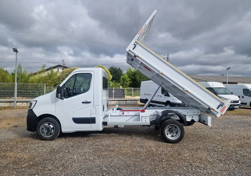 Vue de profil côté gauche d’un Renault Master Benne blanc avec benne basculante levée et roues jumelées arrière.