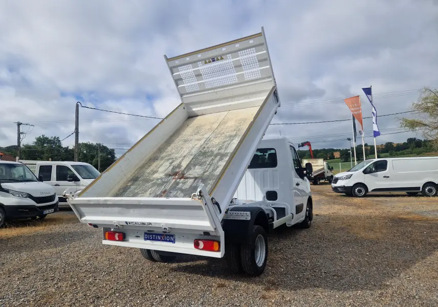 Vue arrière droite d’un Renault Master blanc avec benne relevée et roues jumelées sur un terrain extérieur.