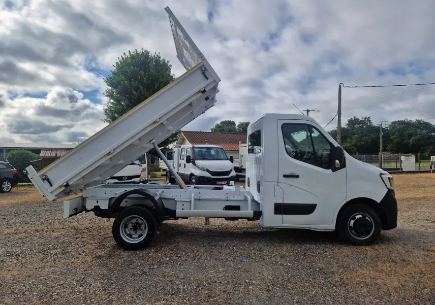 Vue latérale droite d’un Renault Master blanc avec benne relevée et roues jumelées sur terrain extérieur.