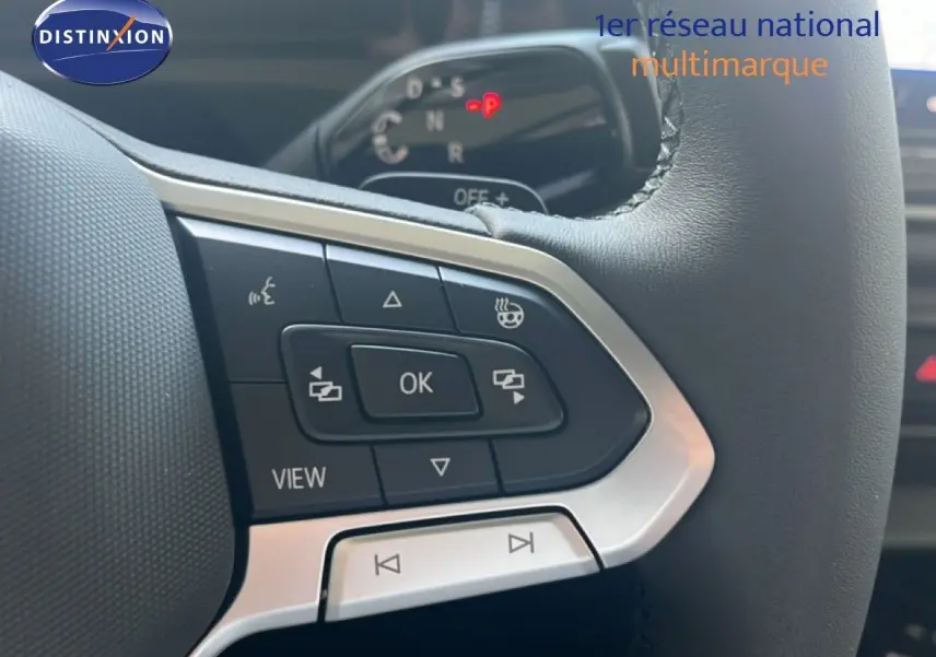 Gros plan sur les commandes gauche du volant noir du Volkswagen Tiguan 2026, avec boutons multifonctions et affichage digital en arrière-plan.
