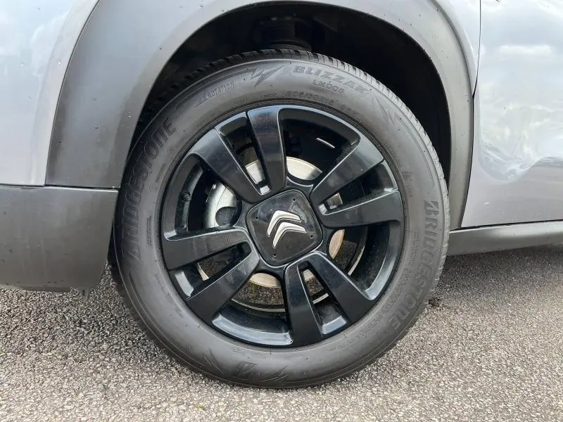 Gros plan sur la roue avant gauche d'une Citroën C3 Aircross gris acier avec jante alliage noire et logo Citroën central.