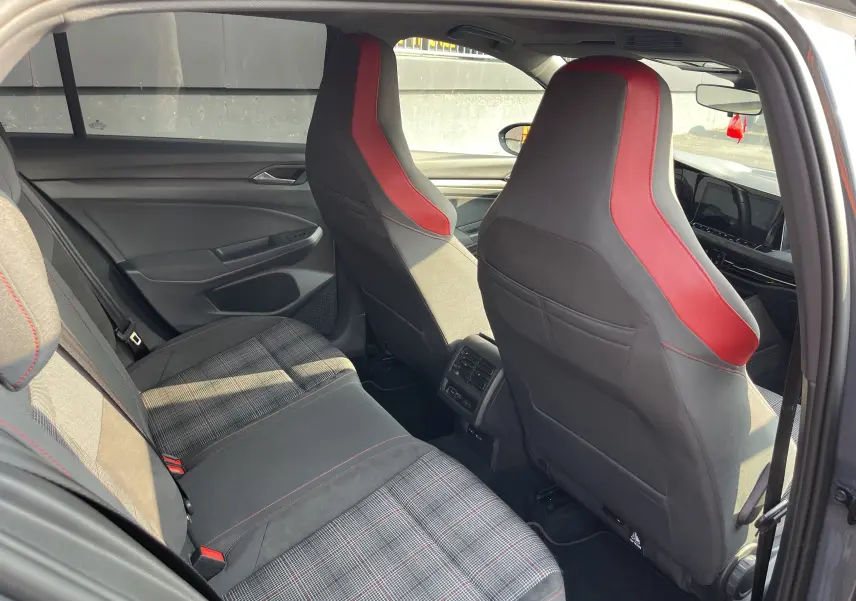 Vue intérieure arrière de la Volkswagen Golf GTI 2021, sièges avant noirs avec bandes rouges et banquette arrière à motif tartan.