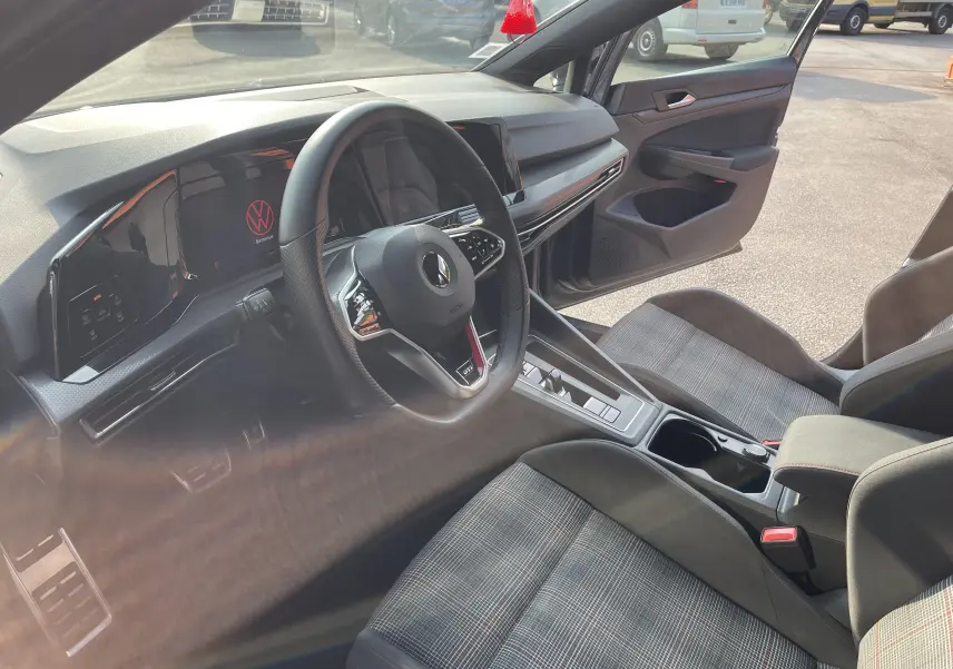 Intérieur de la Volkswagen Golf VIII GTI 2021, vue côté conducteur, sièges tissu à motif écossais et tableau de bord numérique.