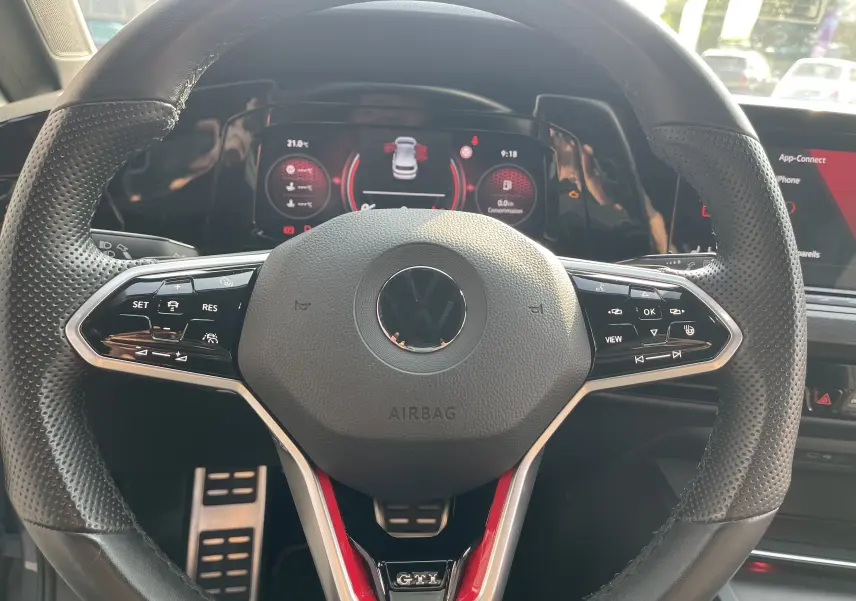 Vue rapprochée du volant cuir noir perforé de la Volkswagen Golf VIII GTI avec logo VW et badge GTI rouge.