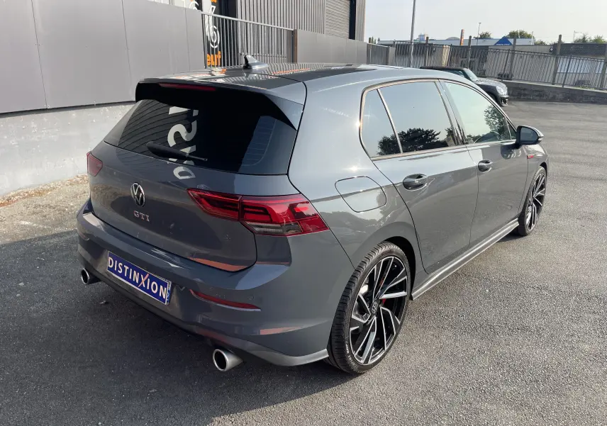 Volkswagen Golf VIII GTI gris vue 3/4 arrière droit, avec jantes sport et double sortie d’échappement chromée.