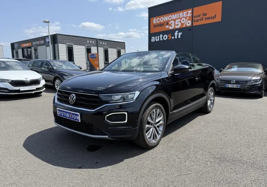 Volkswagen T-Roc Cabriolet noir nacré en 3/4 avant droit sur parking avec jantes alliage et capote ouverte.