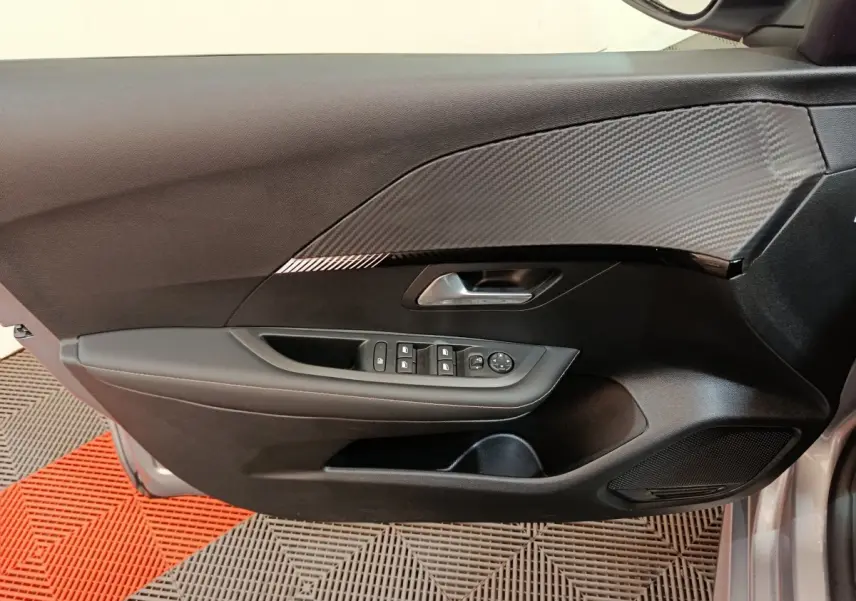 Vue intérieure côté gauche de la porte avant gris clair d'une Peugeot 208 avec commandes électriques et insert décoratif noir.