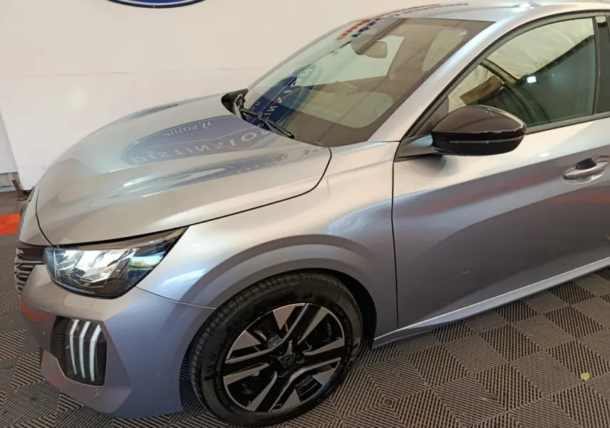Vue 3/4 avant droit d'une Peugeot 208 gris clair avec jantes noires et rétroviseur ton caisse.