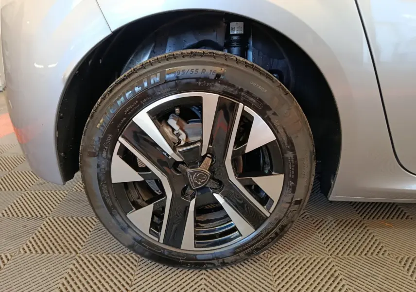 Gros plan sur la roue avant droite gris clair de la Peugeot 208 avec jante alliage bicolore et logo lion central.