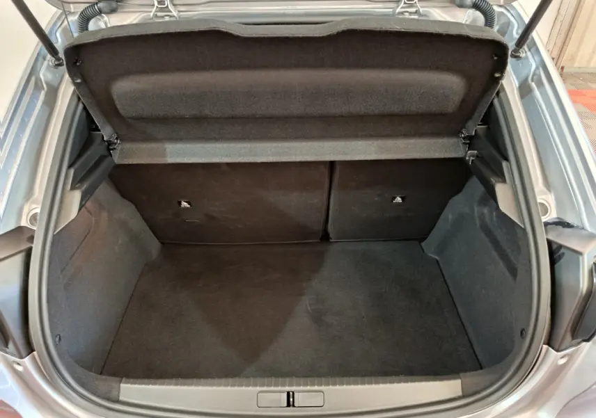Coffre ouvert vu de l'arrière d'une Peugeot 208 gris clair, montrant l'espace de chargement vide et la tablette de séparation.