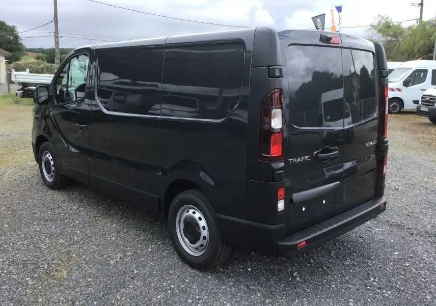 Vue 3/4 arrière droite d’un Renault Trafic Fourgon gris comète avec portes arrière fermées sur un sol gravillonné.