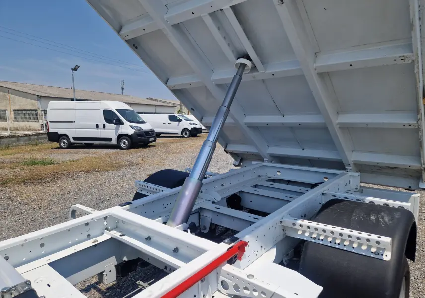 Vue arrière rapprochée du Renault Master blanc avec benne relevée et châssis apparent sous un ciel bleu.