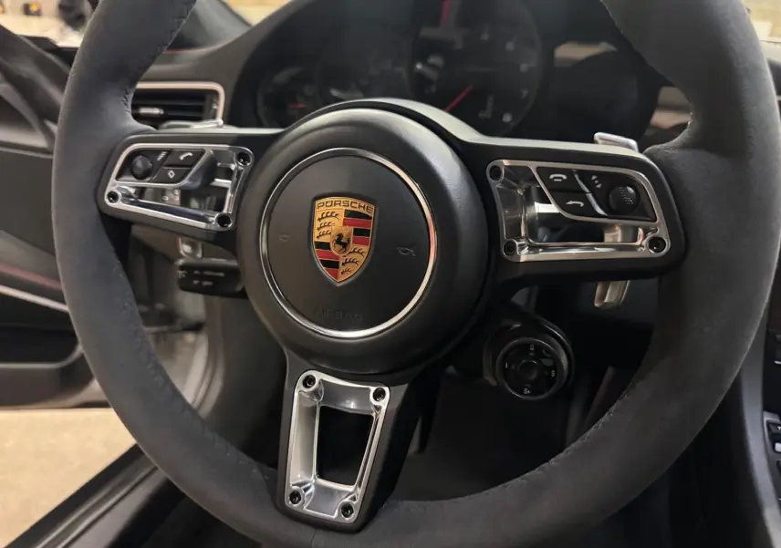 Gros plan sur le volant GT+ en alcantara noir de la Porsche 911 991 2 Carrera T Gris GT Silver, intérieur noir bordeaux.