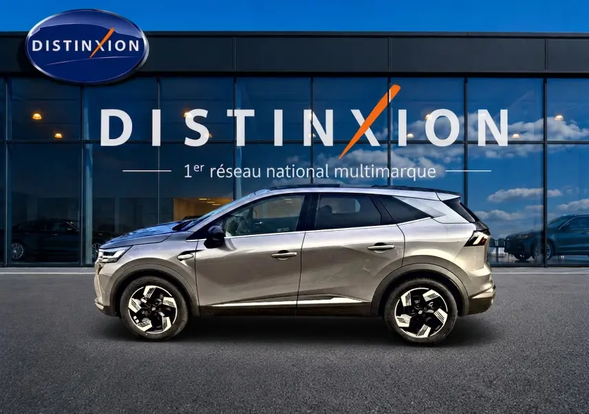 Renault Symbioz gris cassiope en profil droit, SUV hybride 2026 avec jantes alu distinctives devant un showroom Distinxion.