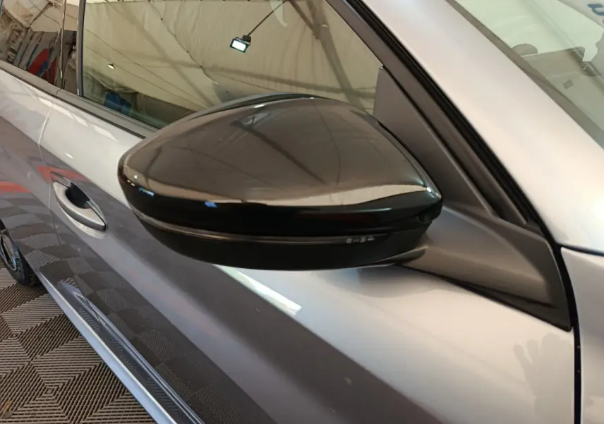 Gros plan sur le rétroviseur noir brillant côté conducteur d'une Peugeot 208 gris clair, vue de profil gauche.