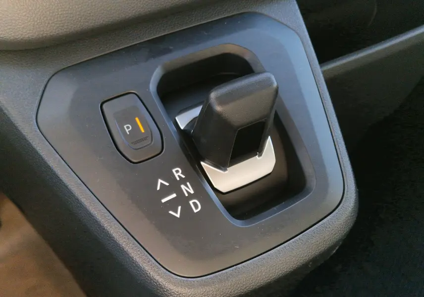 Gros plan sur le levier de vitesses automatique noir du Renault Trafic Fourgon gris Highland, avec bouton parking éclairé.
