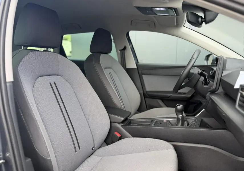 Vue intérieure côté conducteur de la SEAT LEON ST 2025, sièges textile gris clair avec console centrale et volant multifonction.