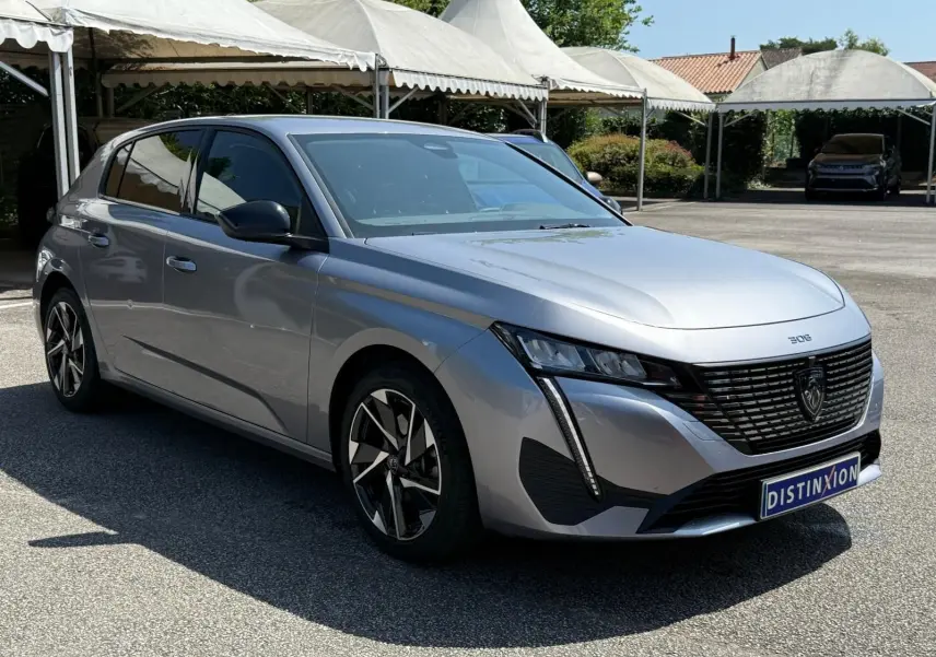 Peugeot 308 gris Artense vue 3/4 avant droit, avec calandre noire et feux LED verticaux distinctifs.