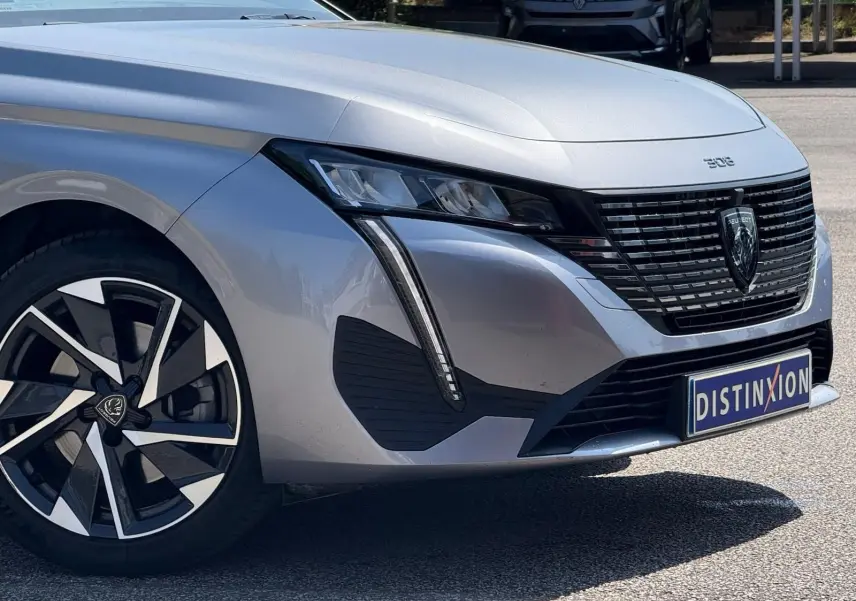 Vue 3/4 avant droit de la Peugeot 308 gris Artense avec calandre noire et jantes alliage distinctives.
