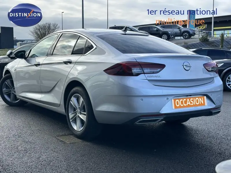 Vue 3/4 arrière droite d'une Opel Insignia Grand Sport blanc glacier avec feux arrière LED et double sortie d'échappement chromée.