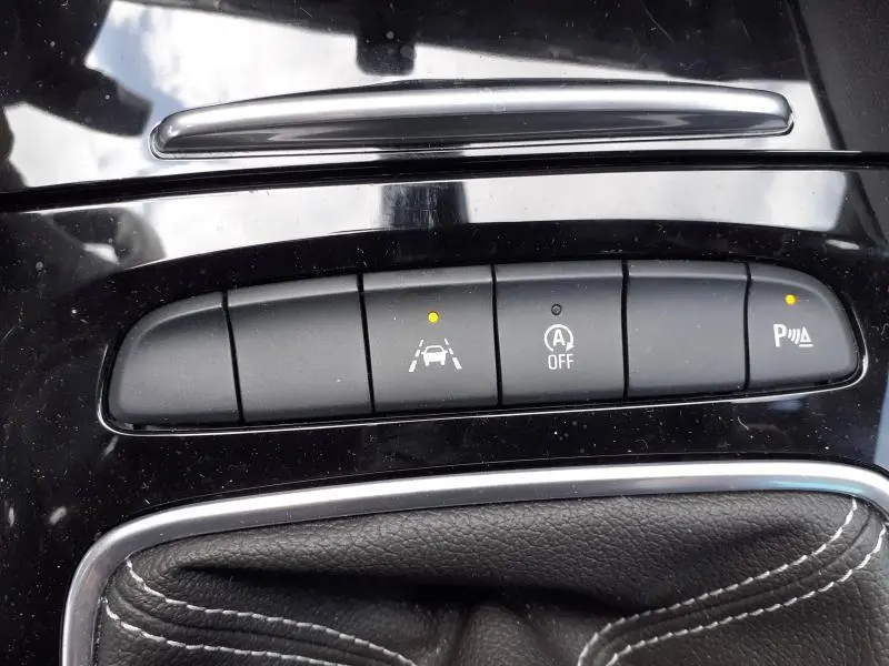 Gros plan sur les commandes d'aide à la conduite de l'Opel Insignia Grand Sport blanc glacier, avec voyants allumés.