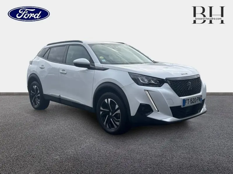 Peugeot 2008 blanc banquise vue 3/4 avant droit, avec jantes alu noires et barres de toit noires.