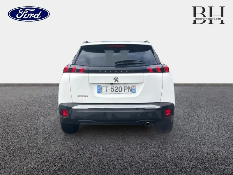 Vue arrière d'un Peugeot 2008 blanc banquise avec feux arrière LED et becquet, sur sol gris uniforme.