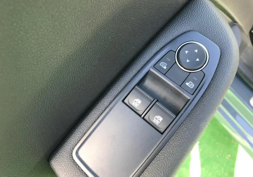 Gros plan sur les commandes des lève-vitres et rétroviseurs côté conducteur d’une Renault Clio 2021 Gris Urban.