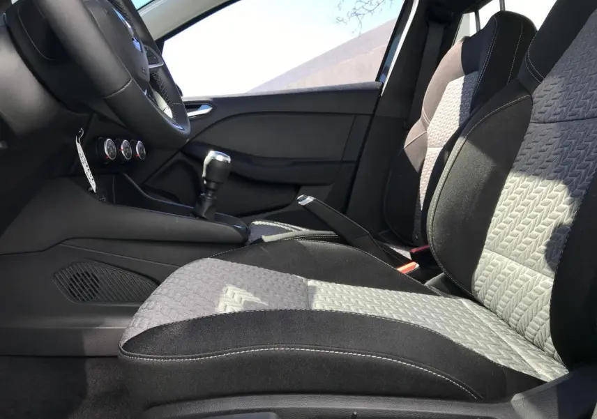 Intérieur avant de la Renault Clio 2021, vue côté gauche sur les sièges tissu noir et gris avec surpiqûres blanches et levier de vitesse manuel.