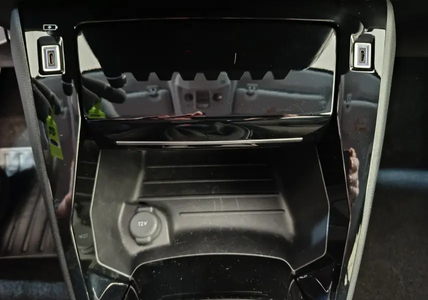 Gros plan sur la console centrale noire brillante du Peugeot 208 PureTech 100 S&S Allure 2025 avec prises USB et prise 12V.