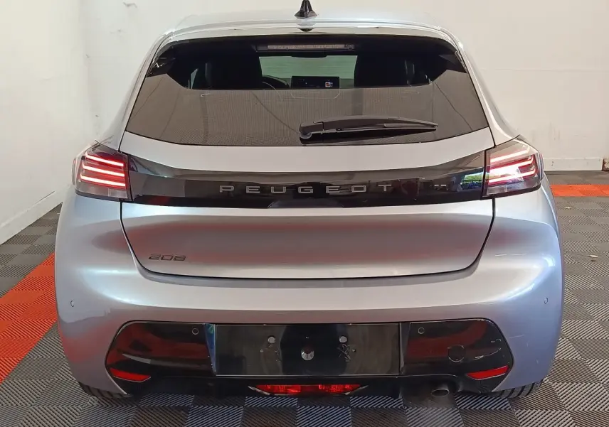 Vue arrière d'une Peugeot 208 gris clair 2025 avec feux arrière LED allumés dans un garage.