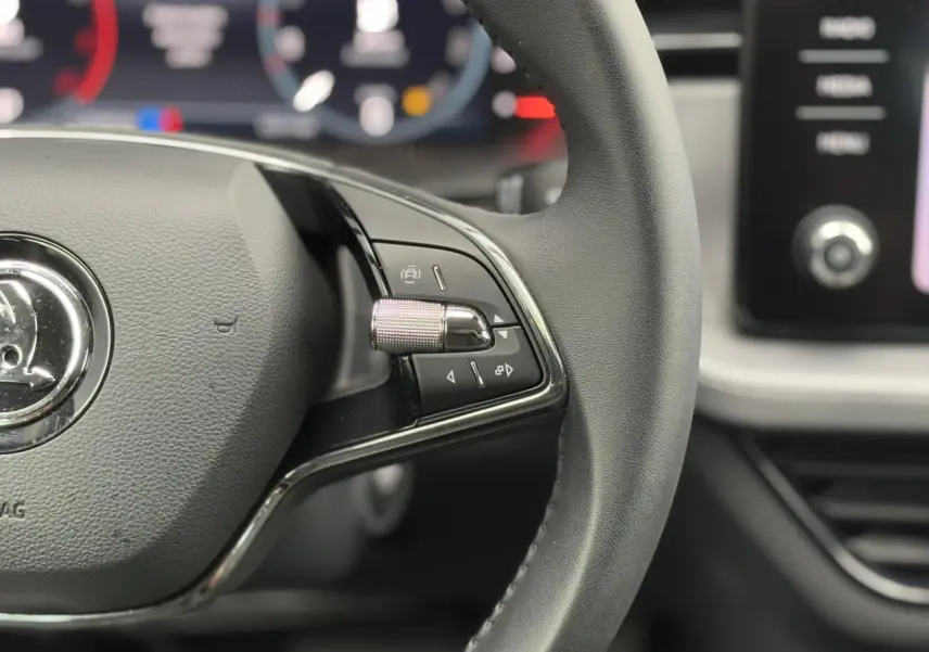 Gros plan sur le volant cuir noir de la Skoda Scala 2024 avec commandes multifonctions côté droit et tableau de bord numérique flou.