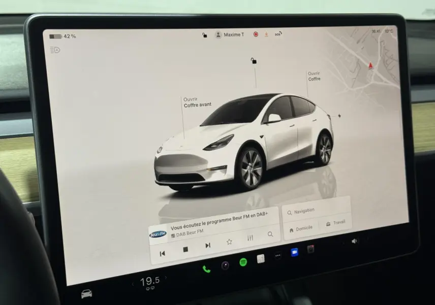 Écran tactile central montrant une Tesla Model Y blanc en 3/4 avant avec options d'ouverture coffre avant et arrière.