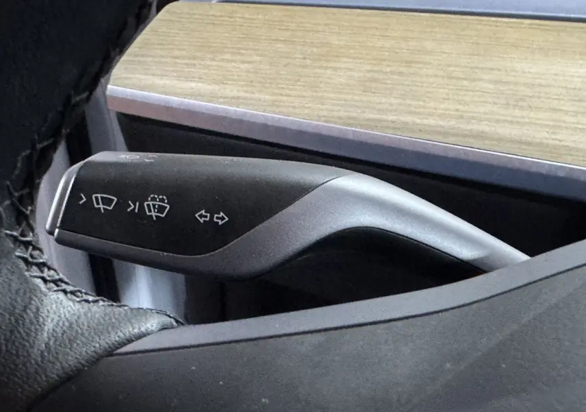 Gros plan sur la commande de clignotants et essuie-glaces du Tesla Model Y blanc, intérieur avec tableau de bord bois.