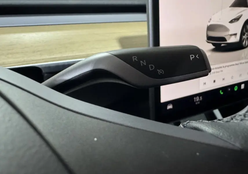 Le levier de vitesses noir de la Tesla Model Y Grand Autonomie visible côté droit, avec écran tactile central en arrière-plan.