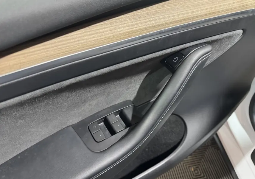 Gros plan sur la garniture intérieure côté conducteur de la Tesla Model Y blanche, avec insert bois et commandes de fenêtres.