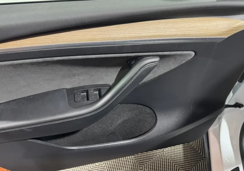 Gros plan sur la porte avant gauche blanche d'une Tesla Model Y, avec garniture noire et insert bois clair.