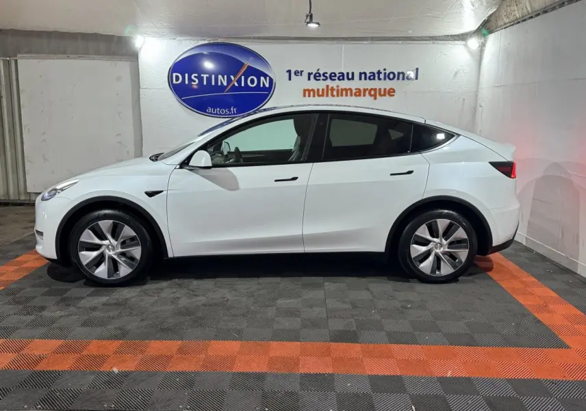 Profil latéral droit d'une Tesla Model Y blanche garée en intérieur avec jantes argentées et vitres teintées.