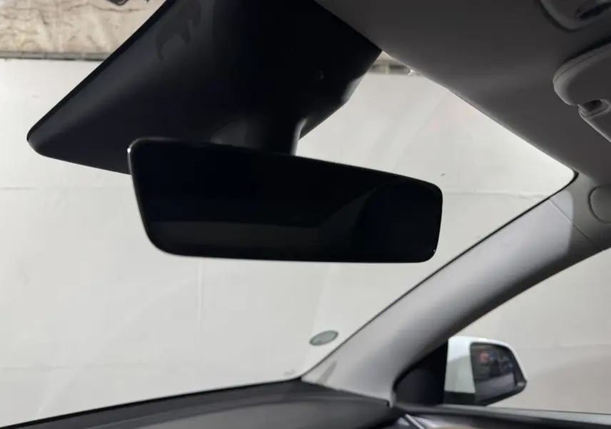 Rétroviseur intérieur noir avec vue partielle du tableau de bord et du montant côté droit d'une Tesla Model Y blanche.