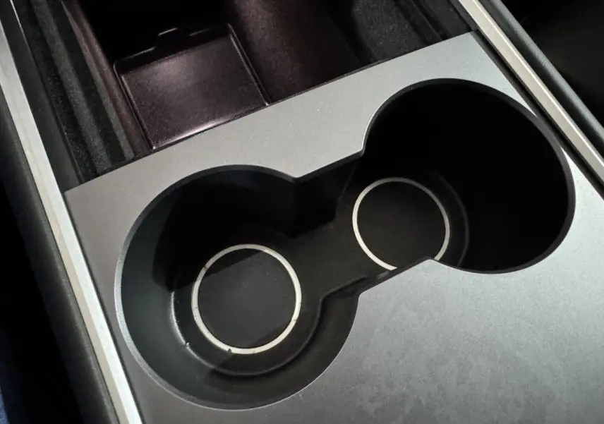 Gros plan sur les porte-gobelets noirs et argentés de la console centrale d'une Tesla Model Y blanche électrique.