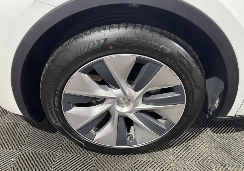 Gros plan sur la roue avant droite d'une Tesla Model Y blanche, avec jante aérodynamique grise et noire.