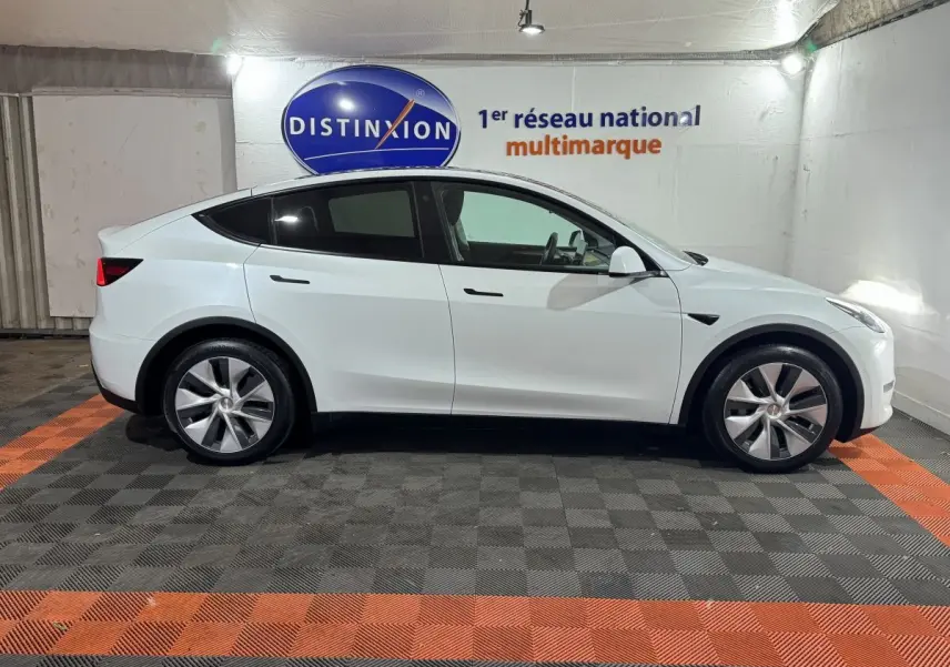 Tesla Model Y blanc en vue profil côté gauche, stationné en intérieur avec logo Distinxion en arrière-plan.