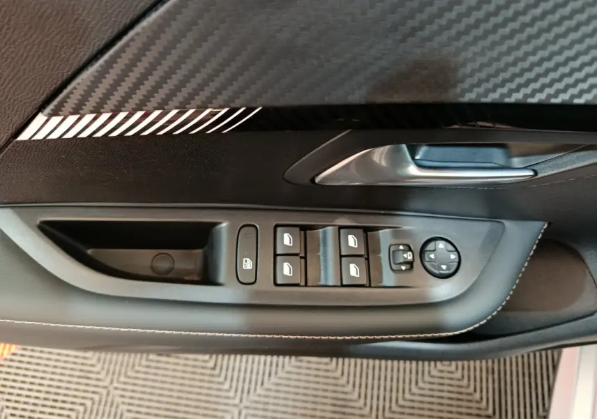 Détail de la commande des vitres et rétroviseurs côté conducteur dans l’habitacle noir d’une Peugeot 208 gris clair.