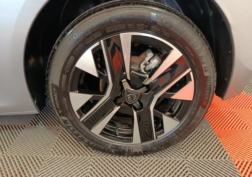 Gros plan sur la roue avant droite d’une Peugeot 208 gris clair avec jante alliage noire et argentée au design moderne.