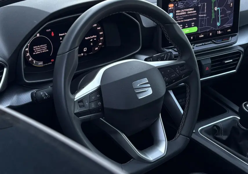 Vue intérieure centrée sur le volant cuir multifonction SEAT, tableau de bord numérique et écran tactile avec navigation.