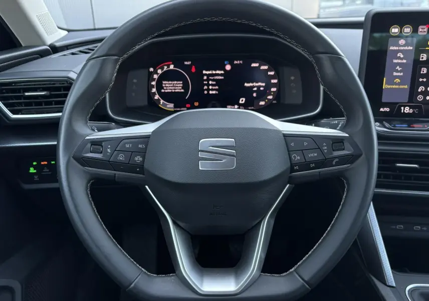 Vue centrée sur le volant cuir multifonction de la SEAT LEON ST 2025 avec tableau de bord numérique et écran tactile.