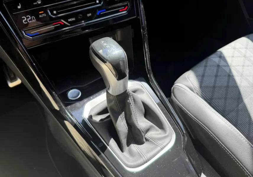 Gros plan sur la commande de boîte automatique et la console centrale noire du Volkswagen T-Roc 2025, siège gris partiellement visible.