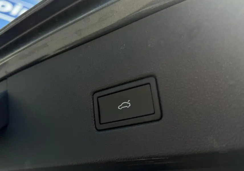 Bouton noir d'ouverture du hayon électrique sur le coffre d'un Volkswagen T-Roc gris Indium, vue rapprochée intérieure.